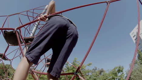 Back-view-of-focused-boy-climbing-rope-attraction-on-playground